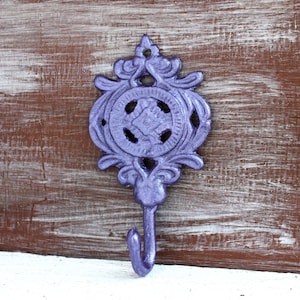 May include: A purple metal hook with a decorative design. The hook has a circular design with a floral pattern and a single hook at the bottom.