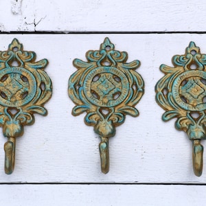 May include: Three ornate gold and teal wall hooks with a decorative design. Each hook has a circular center with a diamond pattern.
