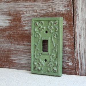 May include: A light green cast iron light switch cover with an ornate floral design.