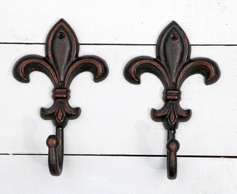 May include: Two black metal hooks with a fleur-de-lis design. The hooks have a dark brown patina finish.