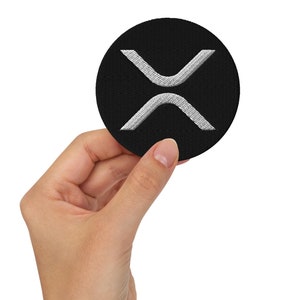 Peut inclure: Un patch rond noir avec un logo en forme de X brodé en blanc.