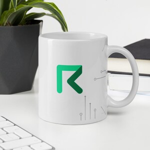 Puede incluir: Taza de cerámica blanca con un logotipo verde y blanco de una letra estilizada "R" con un diseño de circuito impreso. La taza tiene un asa en el lado derecho.