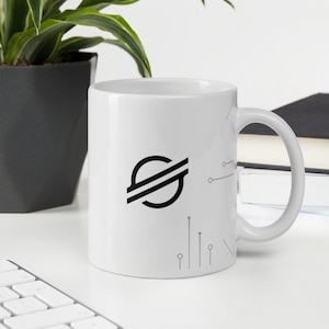 Pode incluir: Caneca de cerâmica branca com um logotipo preto e branco de um planeta com anéis e uma letra S estilizada. A caneca tem um design de circuito cinza no lado.