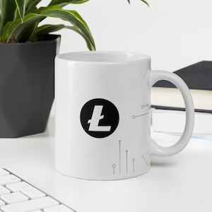 Pode incluir: Caneca de cerâmica branca com um logotipo Litecoin preto e um design de placa de circuito cinza. A caneca está sobre uma superfície branca.