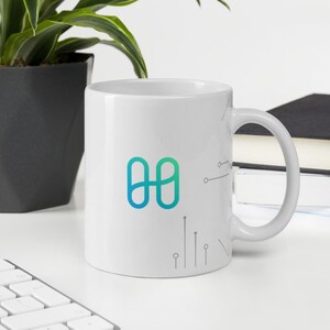 Pode incluir: Caneca de cerâmica branca com um logotipo azul esverdeado de dois círculos sobrepostos com um design de placa de circuito estilizado.