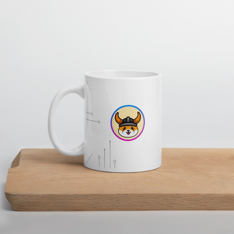 Pu&ograve; includere: Tazza in ceramica bianca con un cane di cartone animato nero e arancione che indossa un elmo vichingo. Il cane &egrave; all'interno di un cerchio con un bordo sfumato rosa e blu. La tazza ha un manico bianco e un design a circuito stampato bianco e nero sul lato.