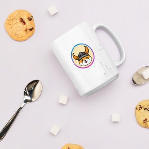 Pu&ograve; includere: Una tazza in ceramica bianca con un'immagine di un cane cartone animato che indossa un elmo vichingo. Il cane &egrave; all'interno di un cerchio con un gradiente giallo, rosa e blu. La tazza ha un manico nero e si trova su una superficie bianca.