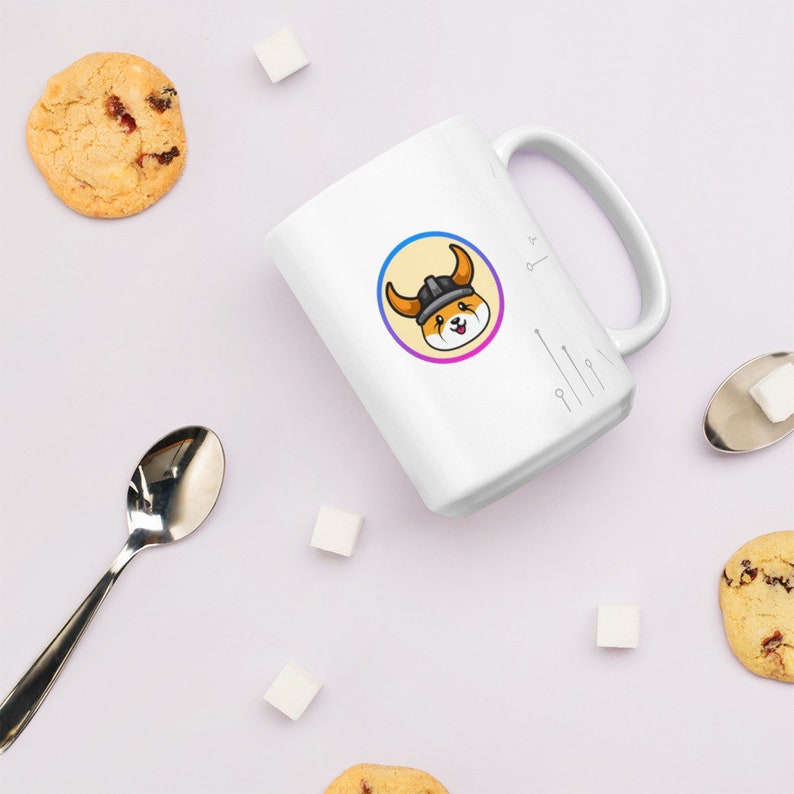 Pu&ograve; includere: Una tazza in ceramica bianca con un'immagine di un cane cartone animato che indossa un elmo vichingo. Il cane &egrave; all'interno di un cerchio con un gradiente giallo, rosa e blu. La tazza ha un manico nero e si trova su una superficie bianca.