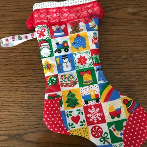 May include: A handmade Christmas stocking with a patchwork design. The stocking features a red lace trim and a white ribbon loop. The patchwork includes various Christmas-themed squares with images of Santa, a snowman, and a Christmas tree.