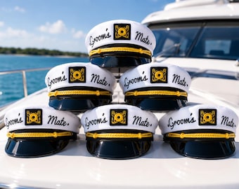 May include: A stack of five white captain hats with black brims and yellow braided trim. Each hat features a black square patch with a yellow anchor emblem and the text Groom's Mate in black script lettering across the front crown.