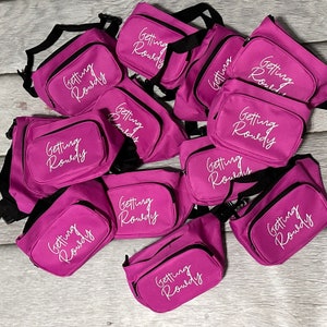 May include: A group of 10 pink fabric bags with black straps and white text that reads "Getting Rowdy".