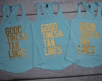 May include: Three light blue racerback tank tops featuring metallic gold text that reads "GOOD TIMES & TAN LINES" followed by "Dana's Bachelorette" in a smaller script font. The sleeveless shirts have a scoop neckline and a curved hemline.