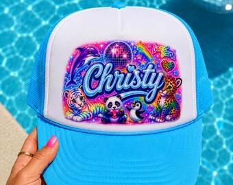 May include: A bright blue trucker hat with a white front panel featuring a colorful Lisa Frank graphic. The design includes a purple dolphin, a rainbow-striped tiger, a panda, a penguin, a leopard, a disco ball, and the name Christy in blue.