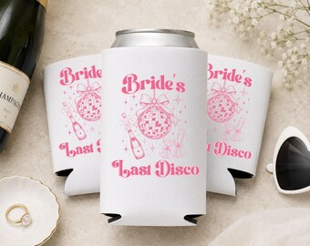 May include: Three white foam can coolers featuring a pink graphic print of a disco ball with a bow, a champagne bottle, and two glasses. The text "Bride's Last Disco" is printed in a bold pink font above and below the central illustration.