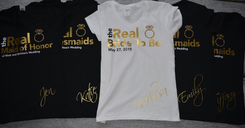 May include: Five black and white t-shirts with gold lettering and a ring design. The shirts say "the Real Maid of Honor", "the Real Bride To Be", and "all bridesmaids".