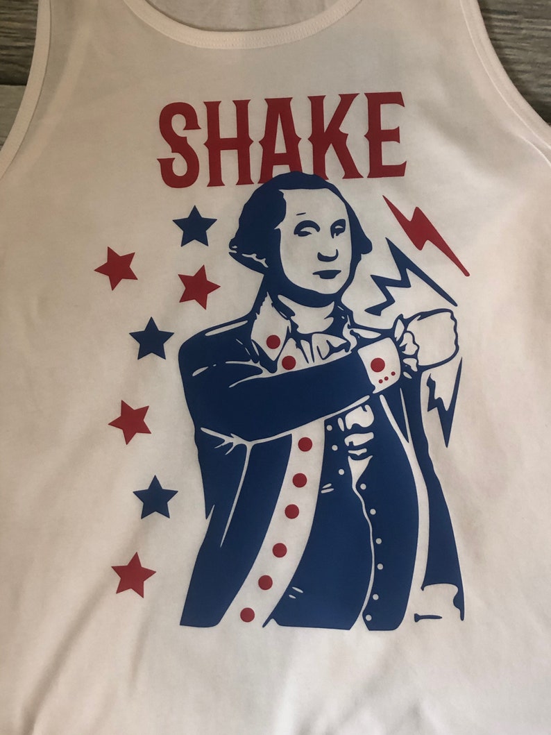 May include: White tank top with a blue and red graphic of a man in a colonial uniform holding a lightning bolt. The text "SHAKE" is printed in red above the graphic. There are red stars around the graphic.