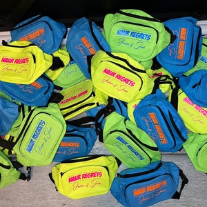 May include: A pile of bright green and blue fanny packs with the text "NAUR REGRETS Jason & Jae" printed on them.