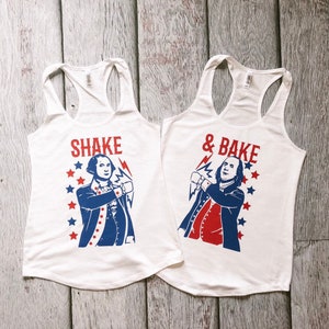 May include: Two white tank tops with a red, white and blue graphic of a man in a colonial outfit. The text on the left tank top says "Shake" and the text on the right tank top says "& Bake".