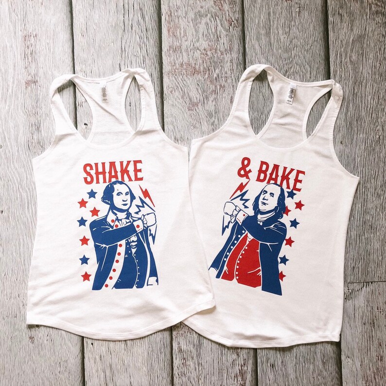 May include: Two white tank tops with a red, white and blue graphic of a man in a colonial outfit. The text on the left tank top says "Shake" and the text on the right tank top says "& Bake".