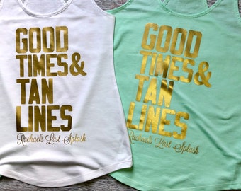 May include: A white tank top and a light green tank top, each featuring the gold metallic text GOOD TIMES & TAN LINES and the script text Rachael's Last Splash printed on the front in a bold, block-style font for the main phrase.