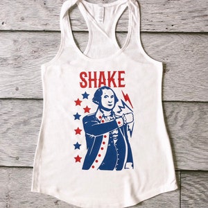 May include: White tank top featuring a blue and red graphic of George Washington holding a lightning bolt and the text "SHAKE".