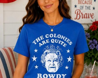 May include: A royal blue short-sleeve t-shirt featuring a white graphic print of Queen Elizabeth II centered within a circle of stars. The text above the portrait reads THE COLONIES ARE QUITE and the text below the portrait reads ROWDY TODAY.