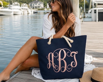 May include: A navy blue canvas tote bag featuring thick, cream-colored rope handles and a large, decorative rose gold monogram with the letters ABT in a cursive, swirling script centered on the front of the bag.