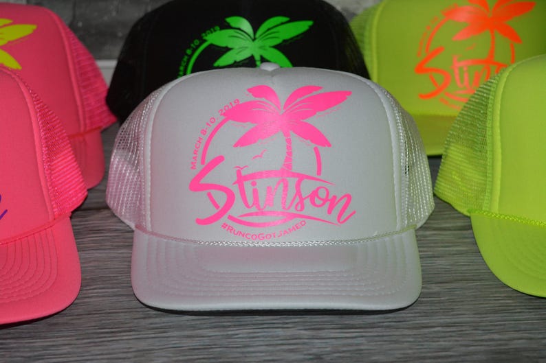 A collection of colorful baseball caps, including a white cap with a pink palm tree design and the word "Stilton" printed on it.