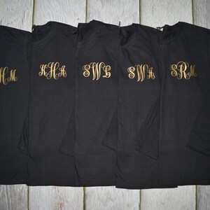 May include: Five black long-sleeve shirts with gold embroidered monograms. The monograms are "CHM", "KHA", "SWL", "SWA", and "SRM".