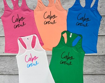 May include: Five tank tops in different colors with the text "Cabo crew" written in black on each. The tank tops are pink, peach, blue, white, and green.