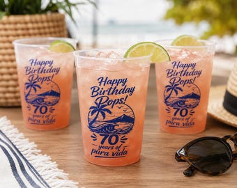 May include: Three clear plastic cups filled with a pink beverage, ice, and a lime wedge. Each cup features blue text reading Happy Birthday Pops! 70 years of pura vida, accompanied by a graphic illustration of a palm tree, ocean waves, and a mountain.