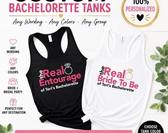 May include: Two racerback tank tops, one black and one white, featuring the text 'the Real Entourage of Tori's Bachelorette' and 'the Real Bride To Be of Tori's Bachelorette' in pink and black with a diamond ring graphic on each shirt.