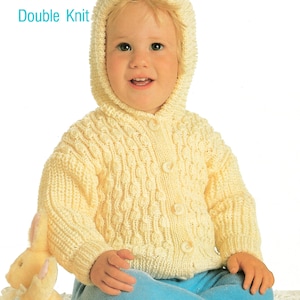 May include: A child in a cream-coloured, hooded knitted cardigan with button fastenings. The cardigan features a textured pattern. The child is also wearing blue trousers. The image includes the text "Peter Pan Double Knit" and "P533 Code C".