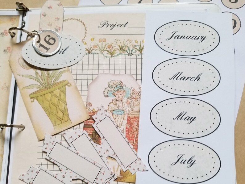 Pode incluir: Uma p&aacute;gina de scrapbook com v&aacute;rios elementos decorativos. Inclui etiquetas ovais com meses, etiquetas com ilustra&ccedil;&otilde;es florais e bot&acirc;nicas e uma etiqueta com o n&uacute;mero 16. A paleta de cores &eacute; suave, com tons bege, creme e pastel.
