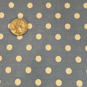 May include: Close-up of blue fabric with a repeating pattern of large, evenly spaced, cream-colored polka dots. A U.S. quarter coin is visible, providing a size reference. The fabric has a textured appearance.