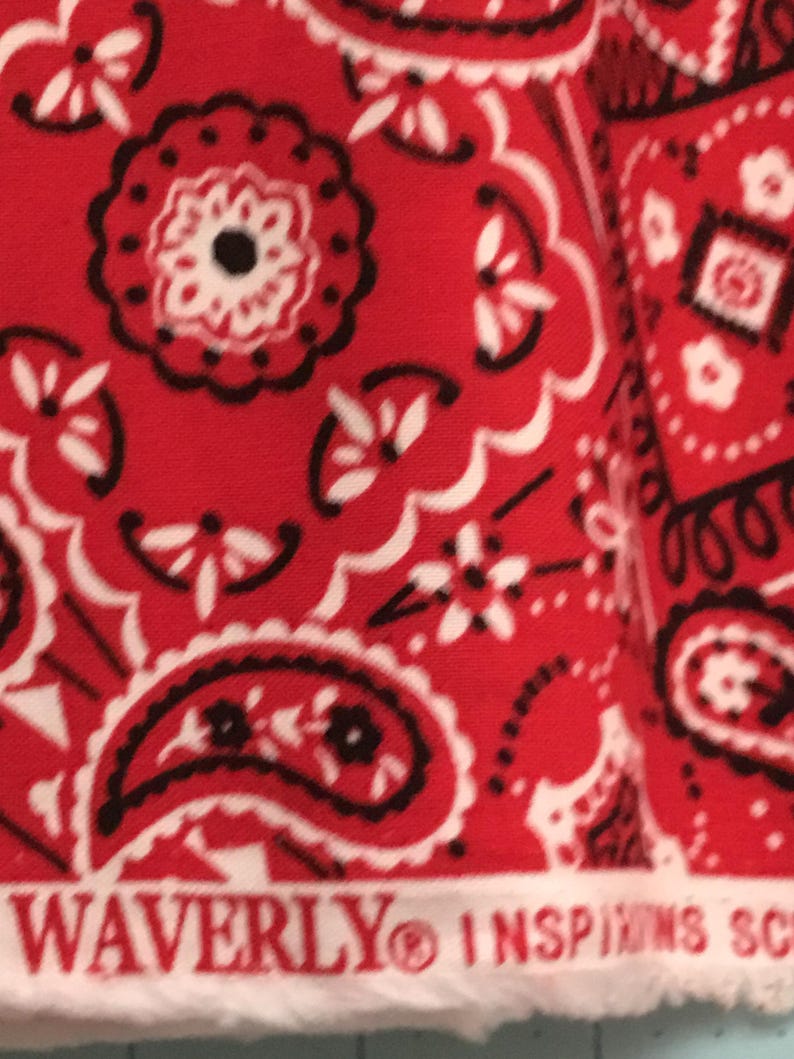 May include: Red fabric with a white and black paisley pattern. The fabric has the text "WAVERLY&reg; INSPIRED SC" printed on the bottom edge.