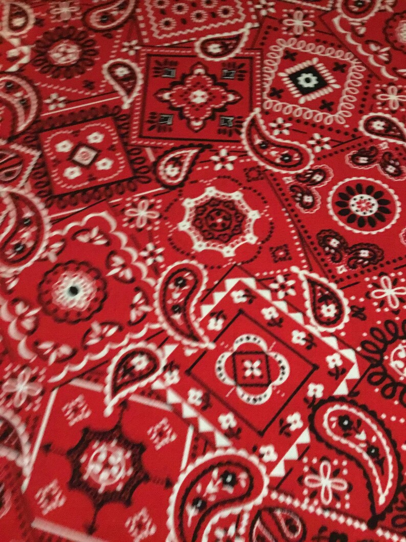 May include: Red bandana fabric with a paisley pattern in white and black. The fabric is a repeating pattern of paisley shapes, diamonds, and small floral designs.