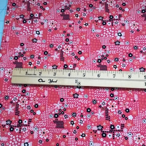 May include: Pink fabric with a white and black floral pattern. The fabric has a repeating pattern of small flowers and leaves. The fabric is 1 yard long.