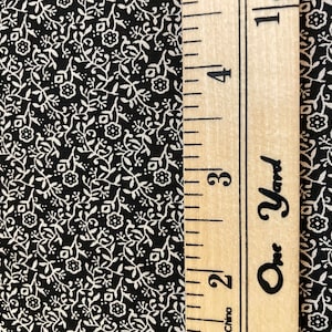 May include: Black fabric with a white floral pattern. A ruler with the words "One Yard" is visible on the right side of the image.