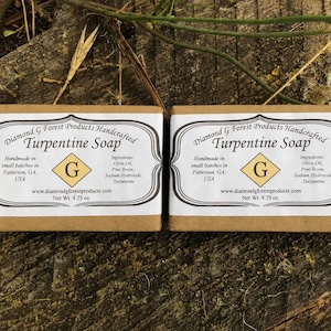 May include: Two rectangular bars of Diamond G Forest Products Handcrafted Turpentine Soap wrapped in brown paper with white labels. The labels feature black text, a yellow diamond with a G, and state a net weight of 4.75 oz per bar.