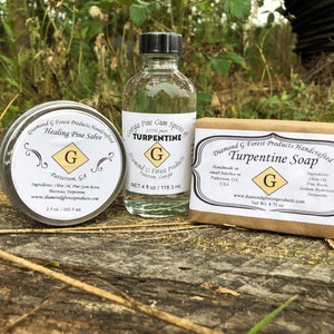 May include: A selection of Diamond G Forest Products, featuring Healing Pine Salve, Turpentine, and Turpentine Soap. The items are presented on a wooden surface against a natural backdrop. Labels display the brand logo and product details.