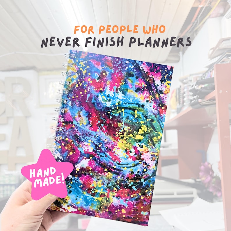 May include: A spiral-bound notebook with a vibrant abstract design in shades of blue, pink, yellow, and purple. The cover features the text "FOR PEOPLE WHO NEVER FINISH PLANNERS." A pink star-shaped sticker with "HAND MADE!" is attached.