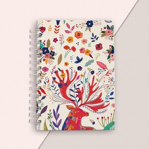 May include: A spiral bound notebook with a white background and a colourful floral pattern featuring a red deer with antlers. The antlers are adorned with flowers and leaves.