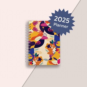 Peut inclure: Un agenda spirale coloré avec un motif floral et le texte "2025 Planner" sur une étoile bleue.