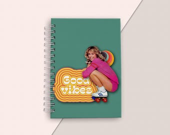 May include: A teal spiral bound notebook with a retro-style sticker featuring a woman on roller skates and the text "Good vibes".