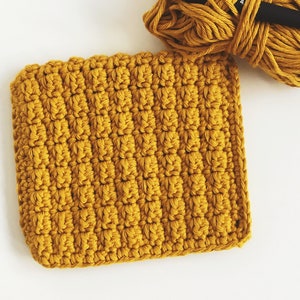 May include: A crocheted square made with mustard yellow yarn, a skein of the same yarn, and a crochet hook.