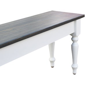 May include: A white bench with a dark gray wood top and turned legs. The bench is made of wood and has a simple, farmhouse style.