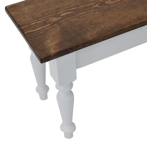 Puede incluir: Un banco de madera con una parte superior de color marr&oacute;n oscuro y patas pintadas de blanco. Las patas tienen un dise&ntilde;o torneado.