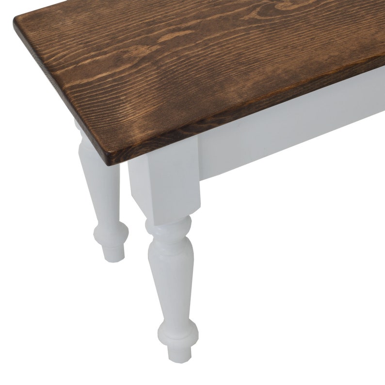Puede incluir: Un banco de madera con una parte superior de color marr&oacute;n oscuro y patas pintadas de blanco. Las patas tienen un dise&ntilde;o torneado.