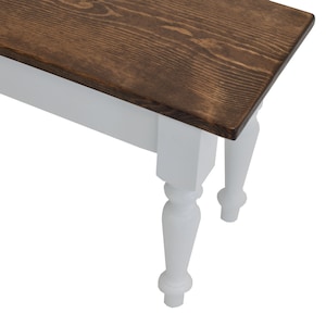 Puede incluir: Un banco de madera con una parte superior de color marr&oacute;n oscuro y patas pintadas de blanco. Las patas tienen un dise&ntilde;o torneado.